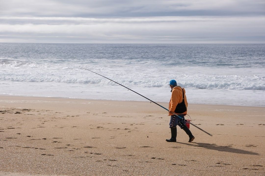 Fiskare med långt spö promenerar längs en vågig kuststrand