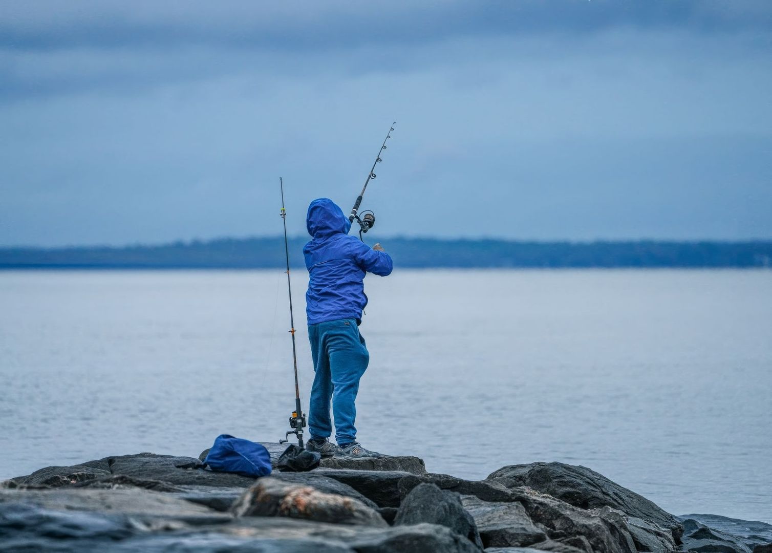 Fiskare i blå regnkläder kastar från klippor vid en kall kust